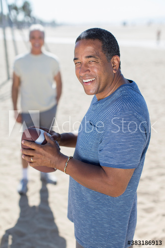 Portrait happy senior man playing football with friend on sunny beach