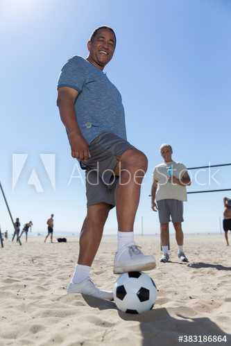 Portrait happy senior man playing soccer on sunny beach
