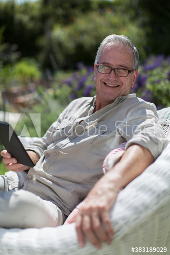 Portrait happy senior man using digital tablet in sunny garden