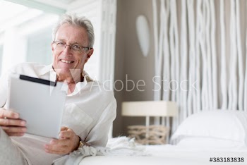 Portrait happy senior man using digital tablet on bed