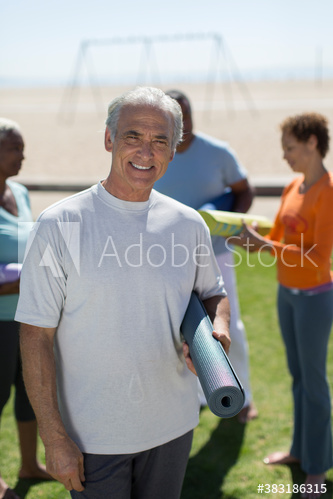 Portrait happy senior man with yoga mat on sunny beach grass