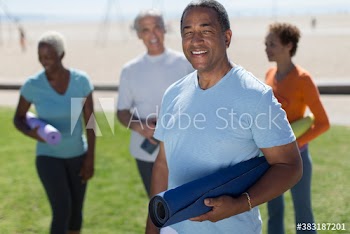 Portrait happy senior man with yoga mat on sunny beach grass