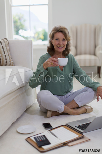 Portrait happy senior woman drinking coffee at laptop on floor