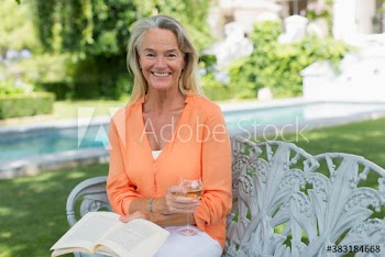 Portrait happy senior woman drinking wine and reading book in garden