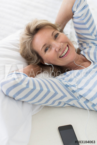 Portrait happy senior woman listening to music with headphones on bed