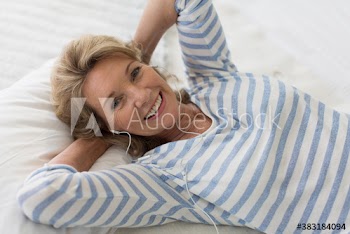 Portrait happy senior woman listening to music with headphones on bed