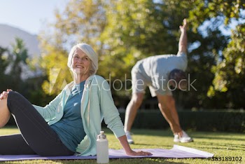 Portrait happy senior woman on yoga mat in sunny park