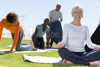 Portrait happy senior woman practicing yoga on sunny grass