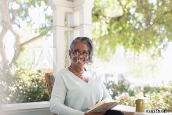 Portrait happy senior woman reading book on sunny porch