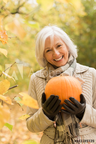 Portrait happy senior woman with pumpkin in autumn park