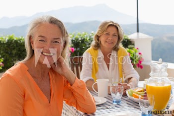 Portrait happy senior women friends enjoying breakfast on sunny patio