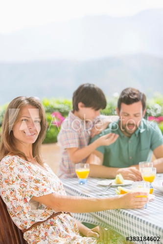 Portrait happy woman enjoying breakfast with family on sunny patio