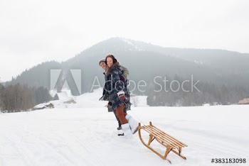 Portrait happy young couple pulling sled in snowy field
