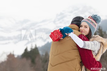 Portrait happy young couple with Christmas gift hugging below mountain