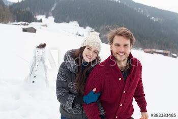 Portrait happy young couple with snowman in snowy field