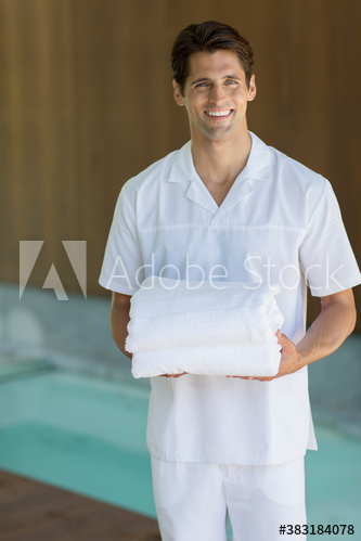 Portrait happy young male masseuse holding towels in spa