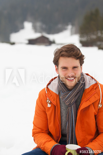 Portrait happy young man drinking hot cocoa in snow