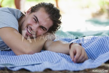 Portrait happy young man relaxing on picnic blanket