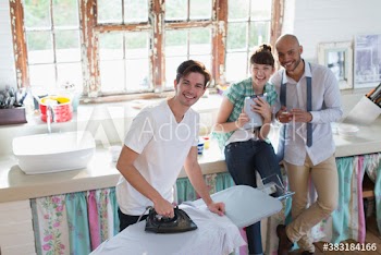 Portrait happy young roommates ironing clothes in kitchen