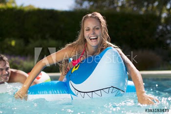 Portrait happy young woman on inflatable shark in sunny swimming pool