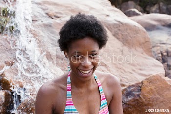 Portrait happy young woman with afro on rocks with waterfall
