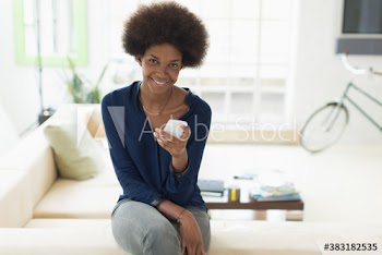Portrait happy young woman with afro using smart phone on sofa