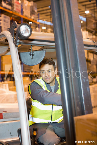 Portrait male worker driving forklift in distribution warehouse
