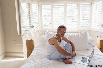Portrait man in pajamas working at laptop on bed