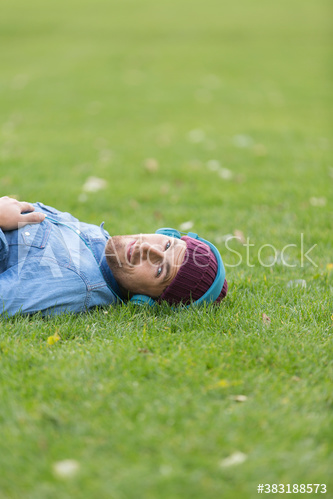Portrait man with headphones listening to music and relaxing in grass