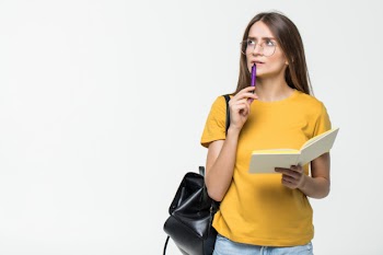 Portrait of a smiling casual girl student with backpack writing in a notepad while standing with books isolated over white wall Free Photo