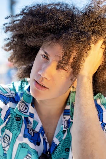 Portrait of Man With Curly Hair Wearing Blue and Teal Collared Top Holding His Head