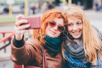 Portrait of smiling young women taking selfie on street