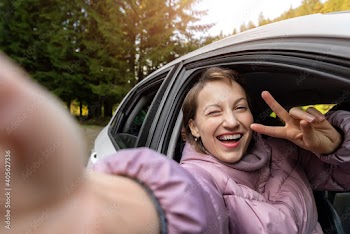 Portrait of young adult beautiful caucasian woman driver enjoy roadtrip adventure traveling by car on mountain nature forest landscape. Happy female person taking selfie photo and winking