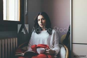 Portrait of young woman holding tea cup sitting on chair at home