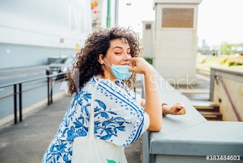 Portrait of young woman removing medical mask while standing outdoors