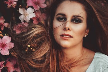 Portrait photo of a woman wearing white top posing beside red and white flowers