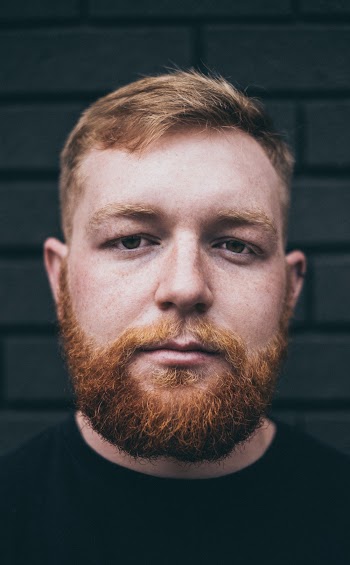 Portrait Photo of Bearded Man Posing In Front of Brick Wall