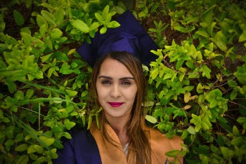 Portrait Photo of Happy Woman in Academic Regalia Standing by Green-leafed Hedge