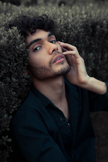 Portrait photo of man wearing a black dress shirt leaning on bushes