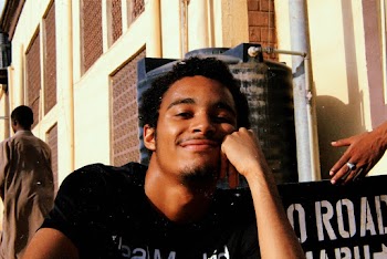 Portrait Photo of Smiling Man Resting His Head on His Left Fist While Sitting In Front Of Building