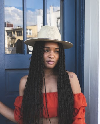 Portrait Photo of Smiling Woman in Red Crop Top and White Hat Standing in Front of Blue Door While Looking Away