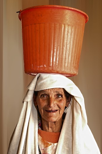 Portrait Photo of Woman Carrying Orange Plastic Pail on Head