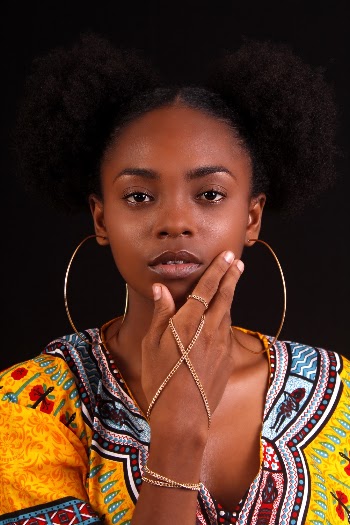 Portrait Photo of Woman in Hoop Earrings and Yellow Dashiki Posing In Front of Black Background