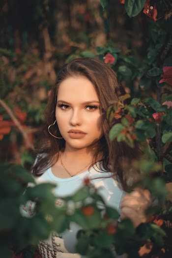 Portrait Photo of Woman in White T-shirt Posing By Green-leafed Plants