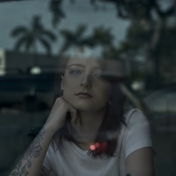 Portrait Photo of Woman Sitting Behind Window Pane With Her Head on Her Hand
