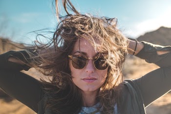 Portrait photo of woman wearing gold-framed sunglasses with her hands behind her head