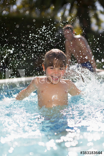 Portrait playful boy splashing in sunny swimming pool