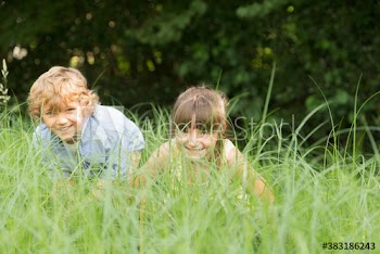 Portrait playful brother and sister hiding in tall grass