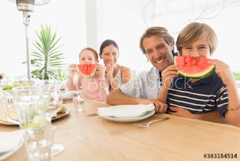 Portrait playful family with watermelon smiles at table