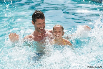 Portrait playful father and daughter splashing in sunny swimming pool